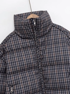 Detail of plaid puffer jacket featuring a stand-up collar and smooth silver metal zipper
