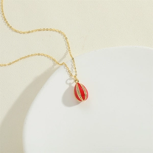 Detail shot of a golden necklace featuring a red enamel drop pendant with zircon inlay