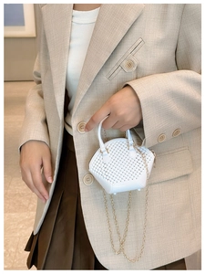 Detailed view of a white woven mini shell bag with a golden metal chain strap