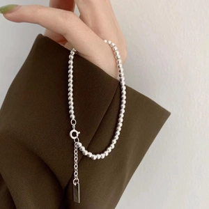 Detail of a minimalist silver beaded bracelet with square pendant on female wrist