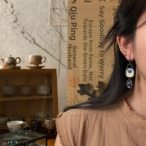 Detail of vintage enamel floral earrings with blue gems worn in a traditional tearoom