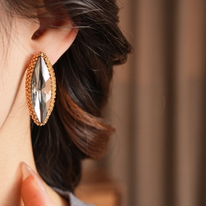 Close-up of model wearing large marquise-shaped crystal earrings with gold beaded edges