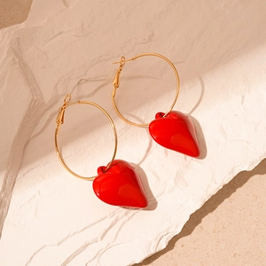Detail of red acrylic heart charms on gold circular hoops resting on a textured stone surface