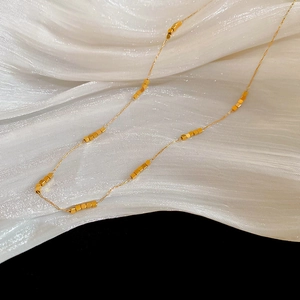 Detailed close-up of golden stainless steel necklace with bead cubes on white fabric
