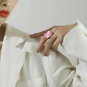 Close-up of a pink enamel irregular ring with gold trim worn by a model in soft lighting