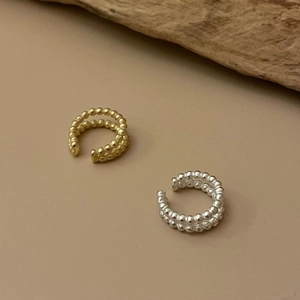 Detail of gold and silver double-layer beaded ear cuffs on a natural wood surface