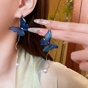 Macro shot of long butterfly tassel earrings with blue charms and white pearls