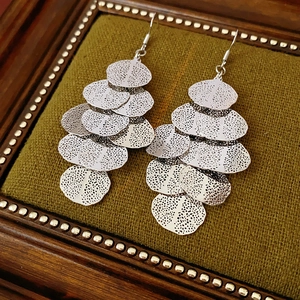 Macro view of silver leaf tassel earrings with layered metal texture on green velvet