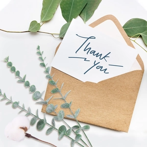 Flat lay of brown kraft envelope with white Thank You card and green eucalyptus leaves