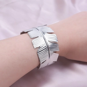 Detailed macro shot of silver leaf-textured wide open cuff bracelet on female wrist