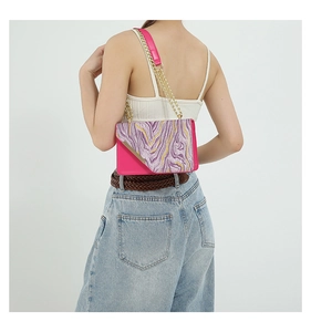 Detail of fuchsia shoulder bag featuring purple marble flap and gold chain strap