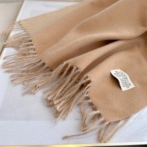 Detailed close-up of beige pashmina scarf fabric texture with fringe and brand label