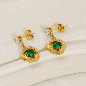 Elegant gold earrings with emerald green zircon and cross-swirl design on silk