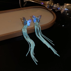 Detail of blue butterfly long tassel earrings with metallic chains on a beige tray