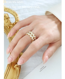 Détail macro d'une bague géométrique dorée avec émail blanc portée par un mannequin