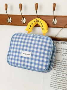 Blaue Kosmetiktasche mit Karomuster und gelbem nummeriertem Griff am Holzhaken
