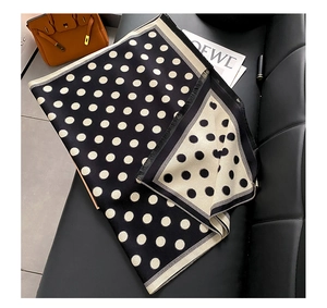 Detail of a retro polka dot scarf with fringes on a leather sofa with a chic orange handbag