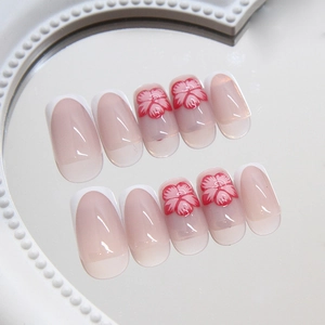 Pink gradient French press-on nails with white tips and red flower patterns on a mirror