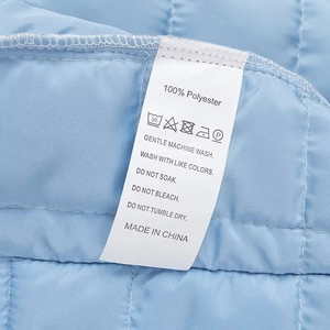 Detailed close-up of garment care label showing 100% polyester on quilted blue floral jacket