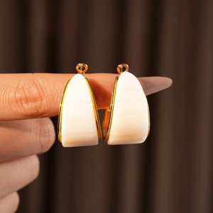 Detail of white triangle resin earring with gold plating held between fingers