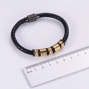 Macro shot of men's braided leather bracelet with gold clasp beside a measuring ruler