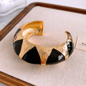 Detail of vintage gold open bangle with black enamel oval and wavy metal texture