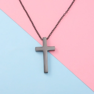 Detailed view of a black metal cross pendant necklace on a soft blue and pink background