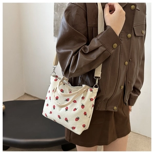 Detail of cream bucket bag featuring red strawberry prints and adjustable shoulder strap