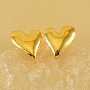 Close-up of golden heart earrings with polished mirror finish on textured glass base