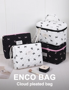 Detail of white quilted toiletry bag with black bow pattern and gold zipper closure