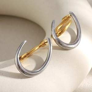Detail of two-tone C-shape earrings in silver and gold metal on a textured display