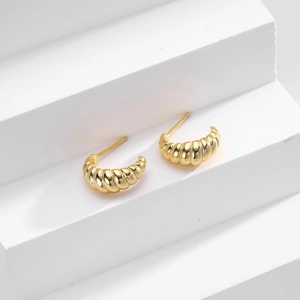 Detailed view of gold twisted croissant earrings on minimalist white display stand