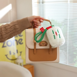 Close-up of plush Mahjong keychain pendant on a brown and beige patchwork handbag