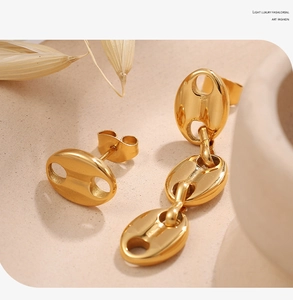 Detailed view of asymmetric gold pig nose earrings with link drop on a warm background