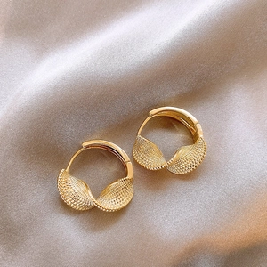 Close-up of golden twisted texture hoop earrings on elegant champagne silk fabric