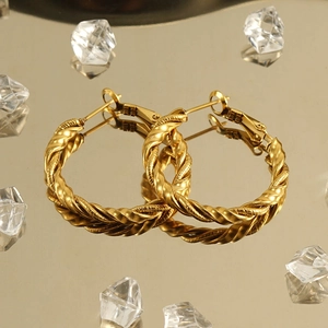 Golden twisted braided hoop earrings in 18k stainless steel on reflective luxury surface