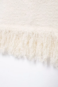 Close-up of off-white tweed knit fabric featuring fringe hem and rich texture detail