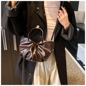 Detail of dark brown ruched cloud bag in glossy leather with handle and strap