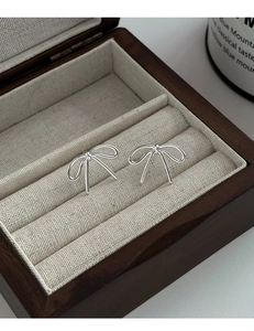 Close-up of elegant silver bow stud earrings presented in a wooden jewelry gift box