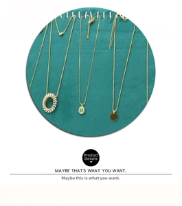 Detailed macro view of 18K gold-plated necklaces on a dark green micro-suede display stand