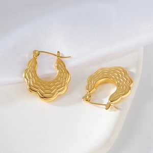 Detailed macro view of gold U-shaped earrings with hammered texture on white silk