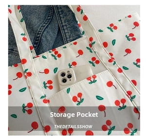 Detailed view of canvas tote bag with cherry prints and front pocket holding a phone
