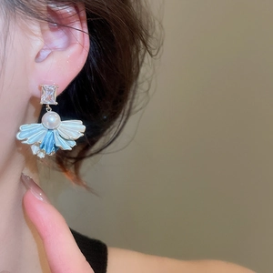 Detail view of model wearing gold-plated earrings with pearl and blue flower petal