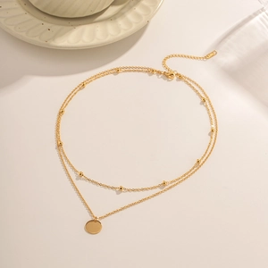 Double-layer 18K gold stainless steel chain necklace with circular pendant on beige surface