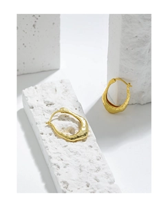 Detail of gold U-shaped earrings with irregular hammered texture on white stone