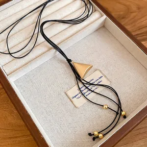 Minimalist black leather cord necklace with matte gold triangle pendant in a wooden box