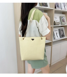 Detailed view of beige woven tote bag with metal chain strap and triangular logo plaque