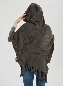 Detail of dark brown knitted poncho showing fringe hem and faux fur hood trim texture