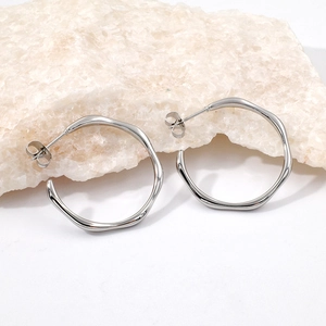Macro shot of silver wavy hoop earrings placed on a white textured natural stone