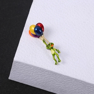 Whimsical green frog enamel brooch holding colorful balloons on a premium metal pin
